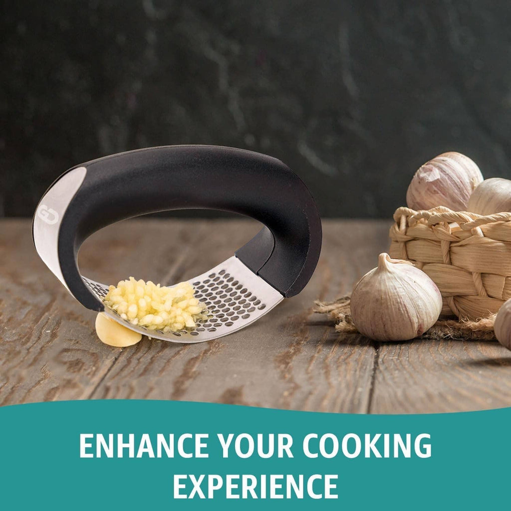 Black garlic press rocker over minced garlic, stainless perforated plate and garlic bulbs