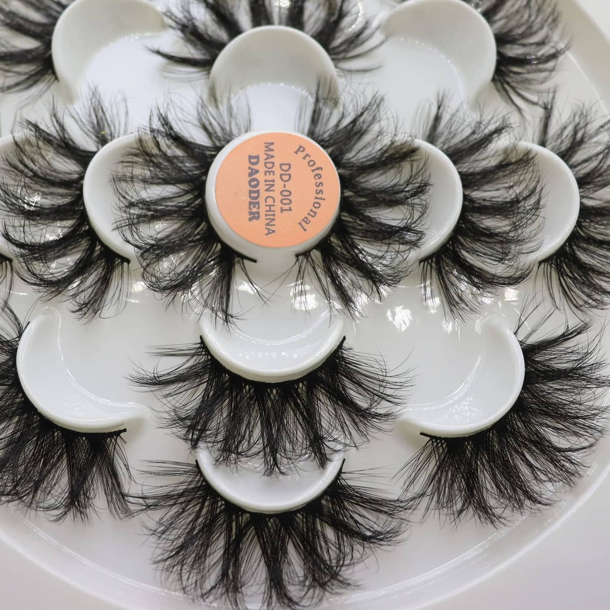 Wispy black false eyelashes with long, full lash clusters on white round trays.