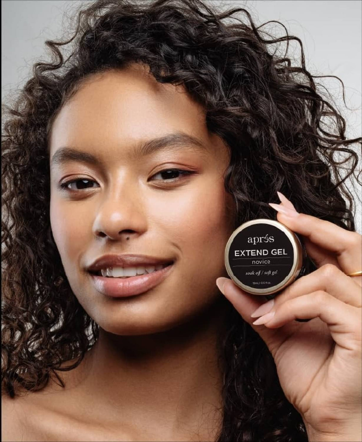 Apres Extend Gel Novice 15 ml clear jar held beside model's face