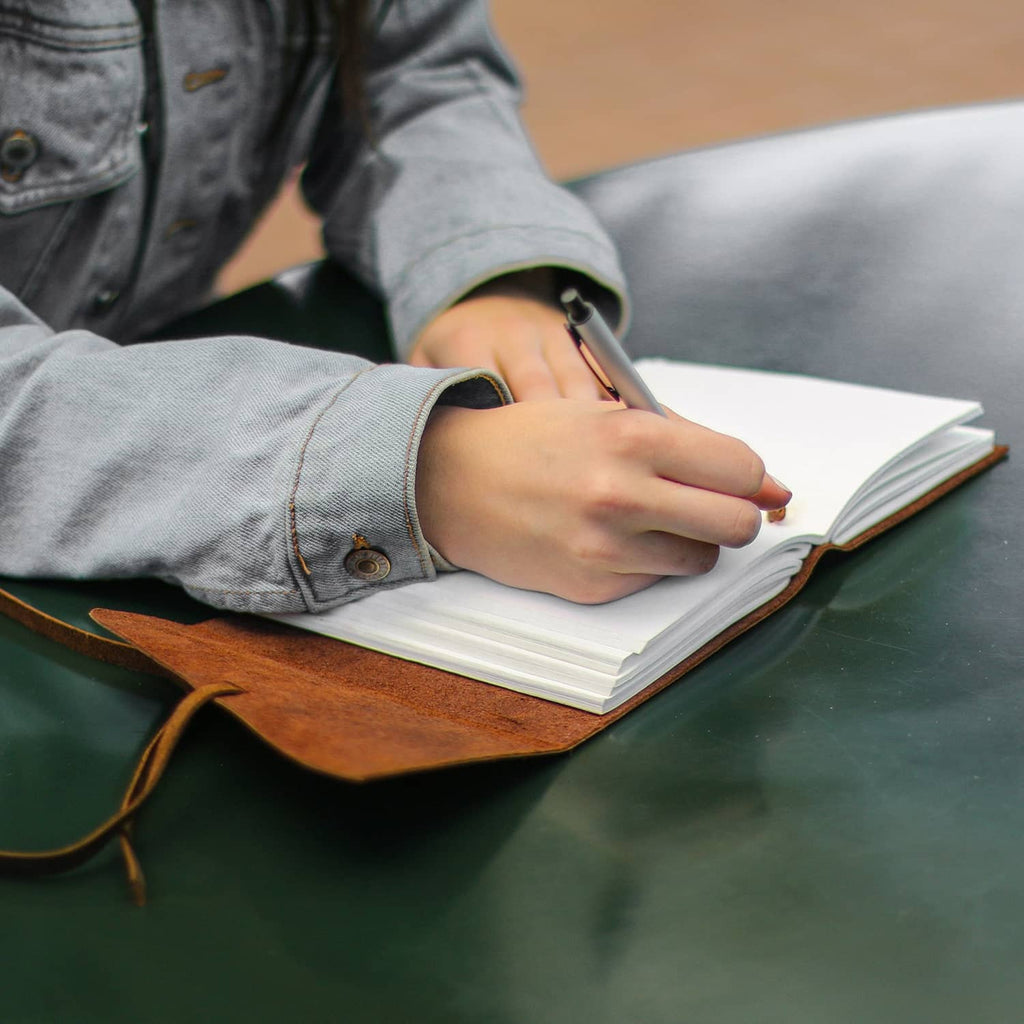 Open brown leather journal notebook with pen writing, pages on tabletop.