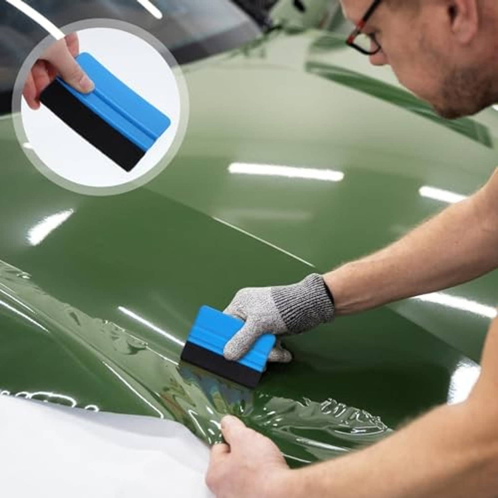 Hand using a blue vinyl squeegee with felt edge to smooth film on a surface.