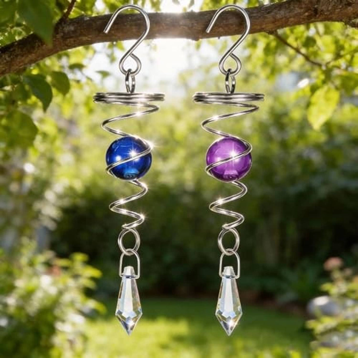 Two hanging stainless steel wind spinners on a branch with blue and purple spheres
