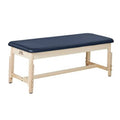 Stationary treatment table with dark blue padded top and light wood frame