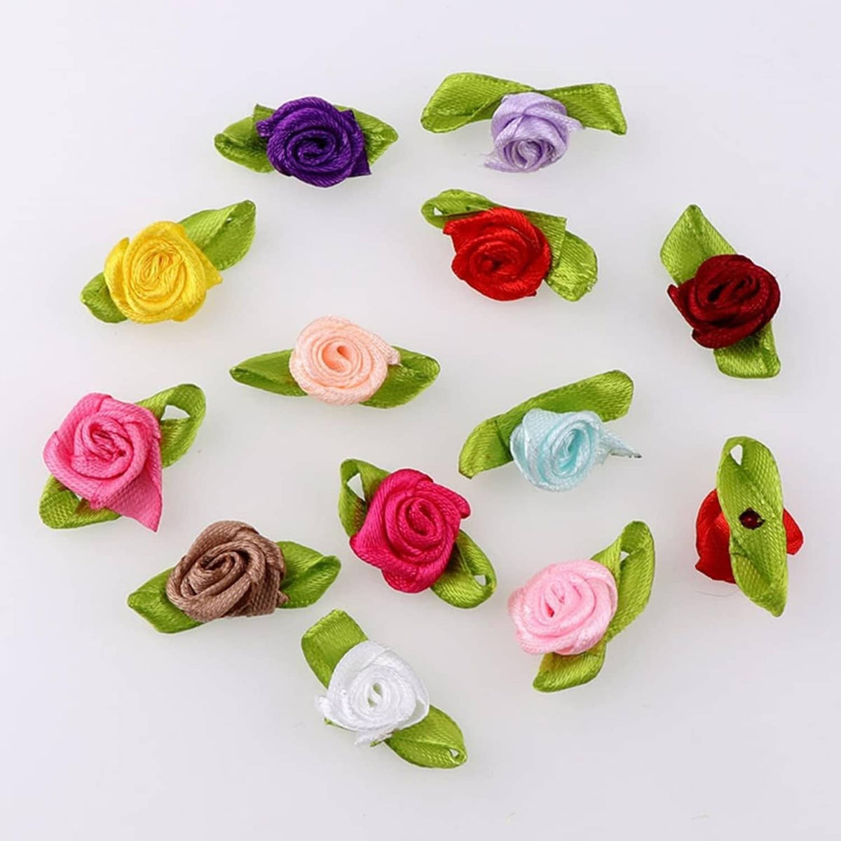 Assorted mini ribbon rose flowers with green leaves, flat lay of multiple colors