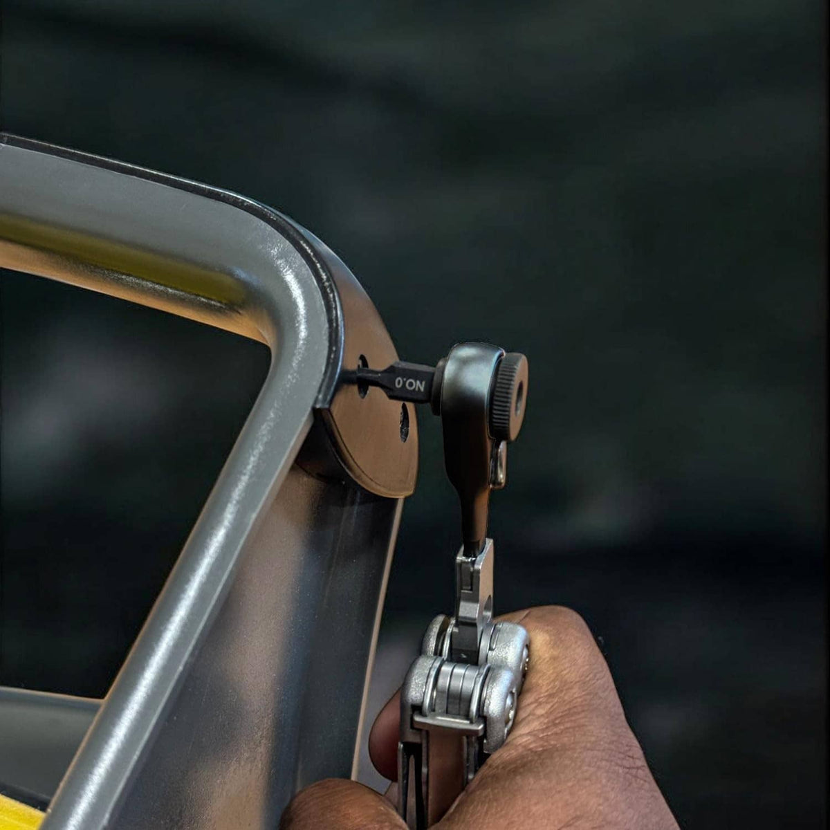 Hand using ratchet bit tool to tighten a metal bracket