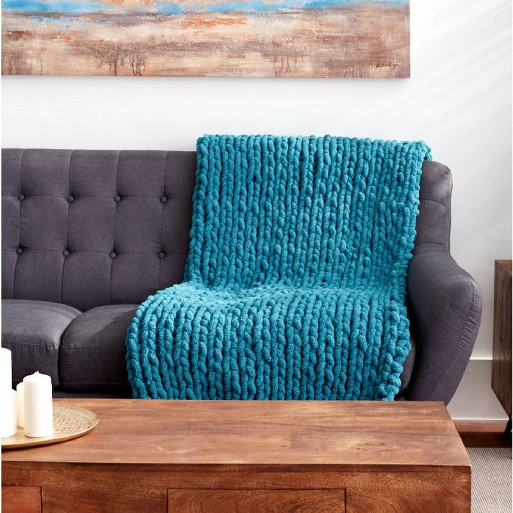 Light teal chunky knit blanket throw folded over a gray sofa