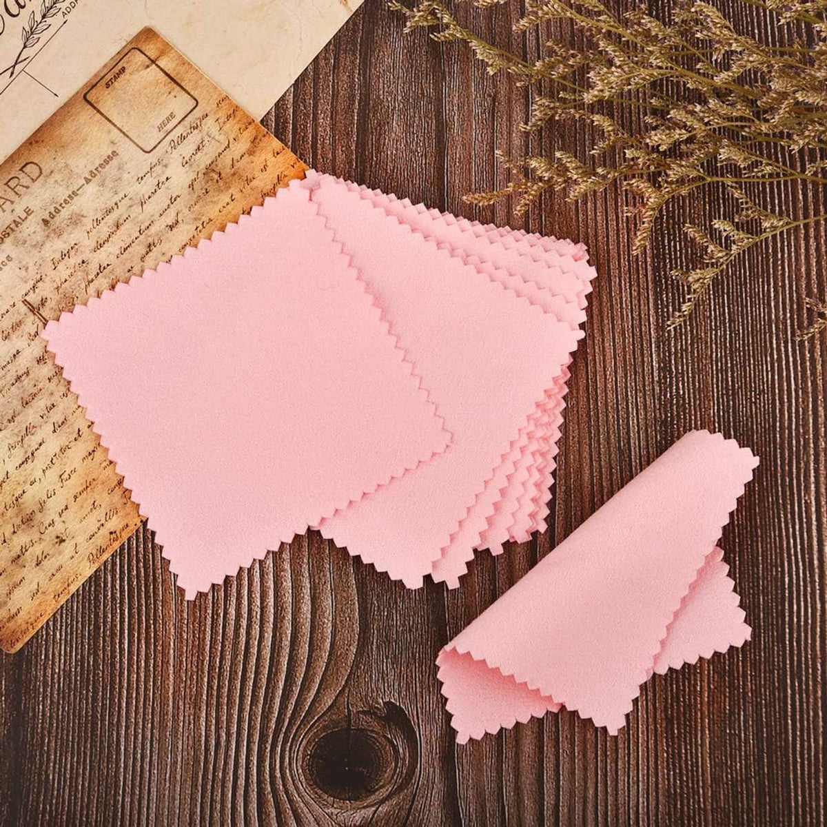Stack of pink jewelry cleaning cloths with serrated edges on wooden surface