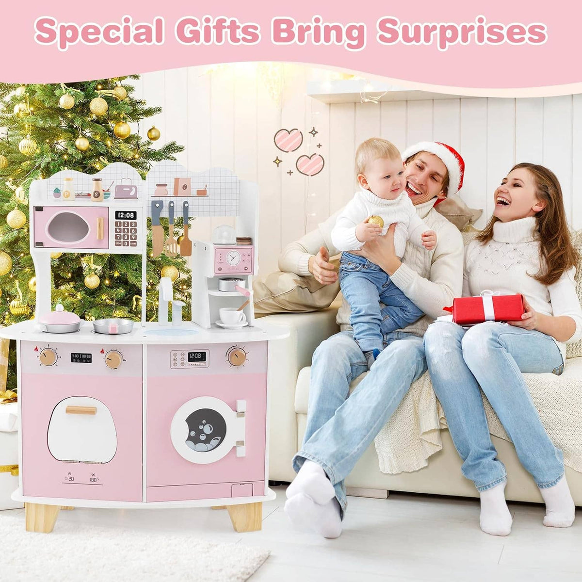 Pink and white wooden play kitchen set next to decorated tree, child and family sitting nearby