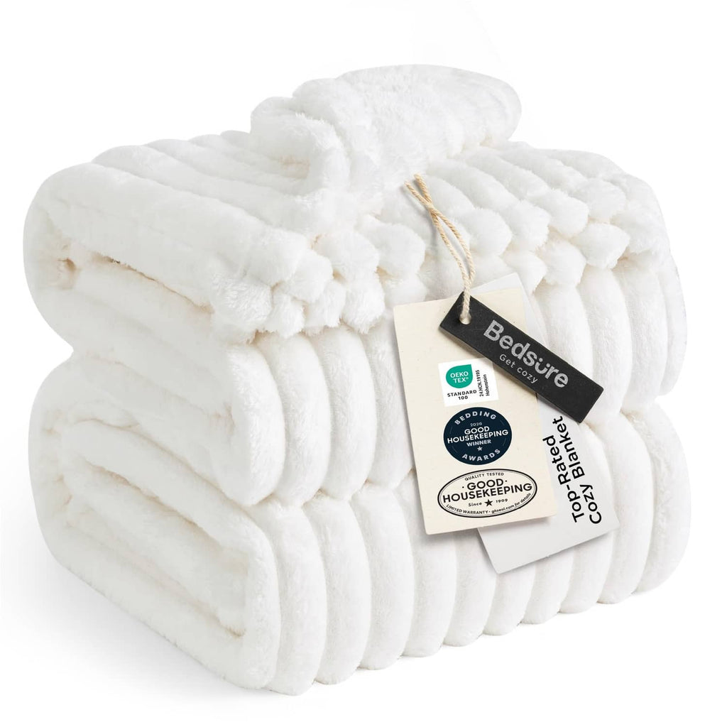 Off-white ribbed fleece blanket with pom-pom trim and folded edge detail