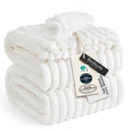 Off-white ribbed fleece blanket with pom-pom trim and folded edge detail