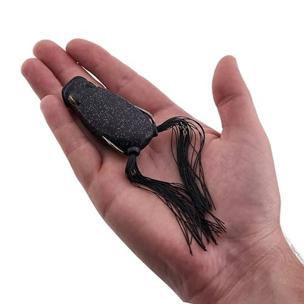 Soft frog lure in hand, dark body with long skirt and hook loops