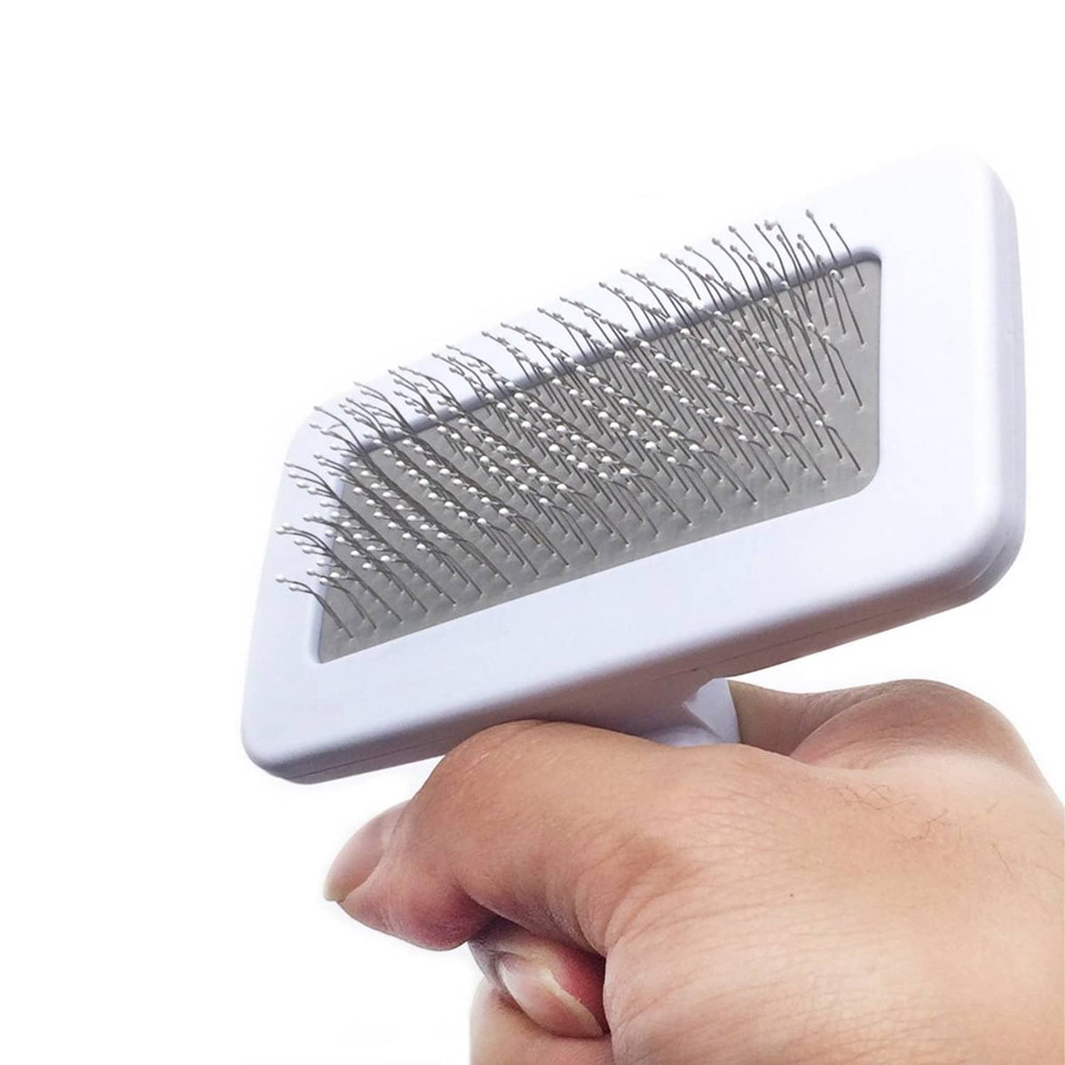 Pet slicker brush close-up in hand, showing dense coated pins on white pad.