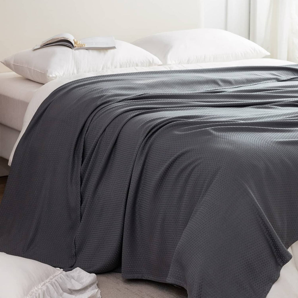 Dark gray cooling blanket spread on a bed, waffle-like textured weave