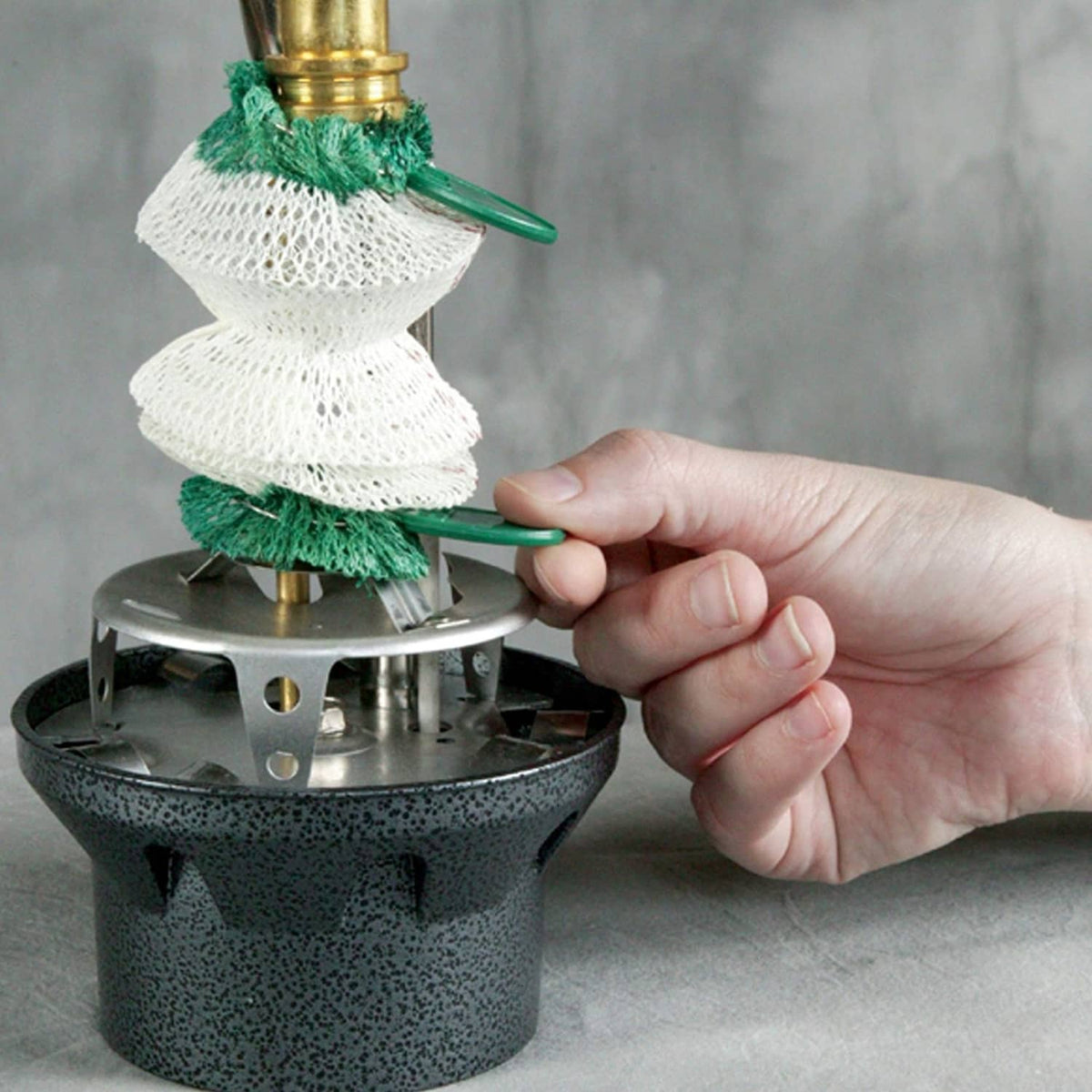 Hand presses green-and-white wick accessory onto Coleman Northstar lantern burner base