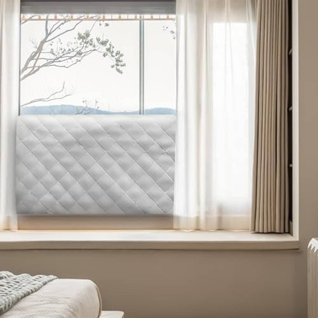 Gray quilted indoor air conditioner cover in a window opening with cord attached.