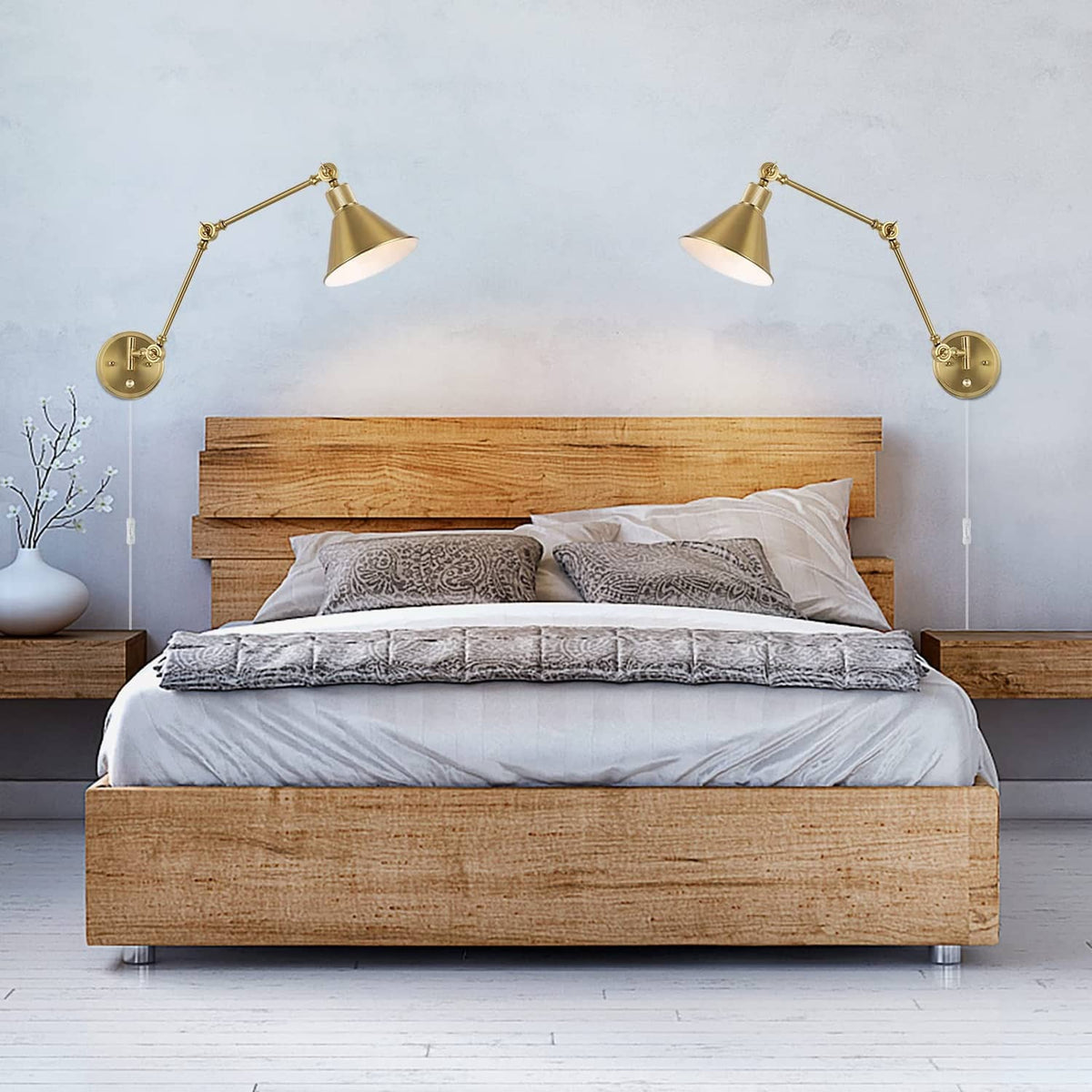 Pair of brushed brass wall sconces with conical shades above wooden bed frame