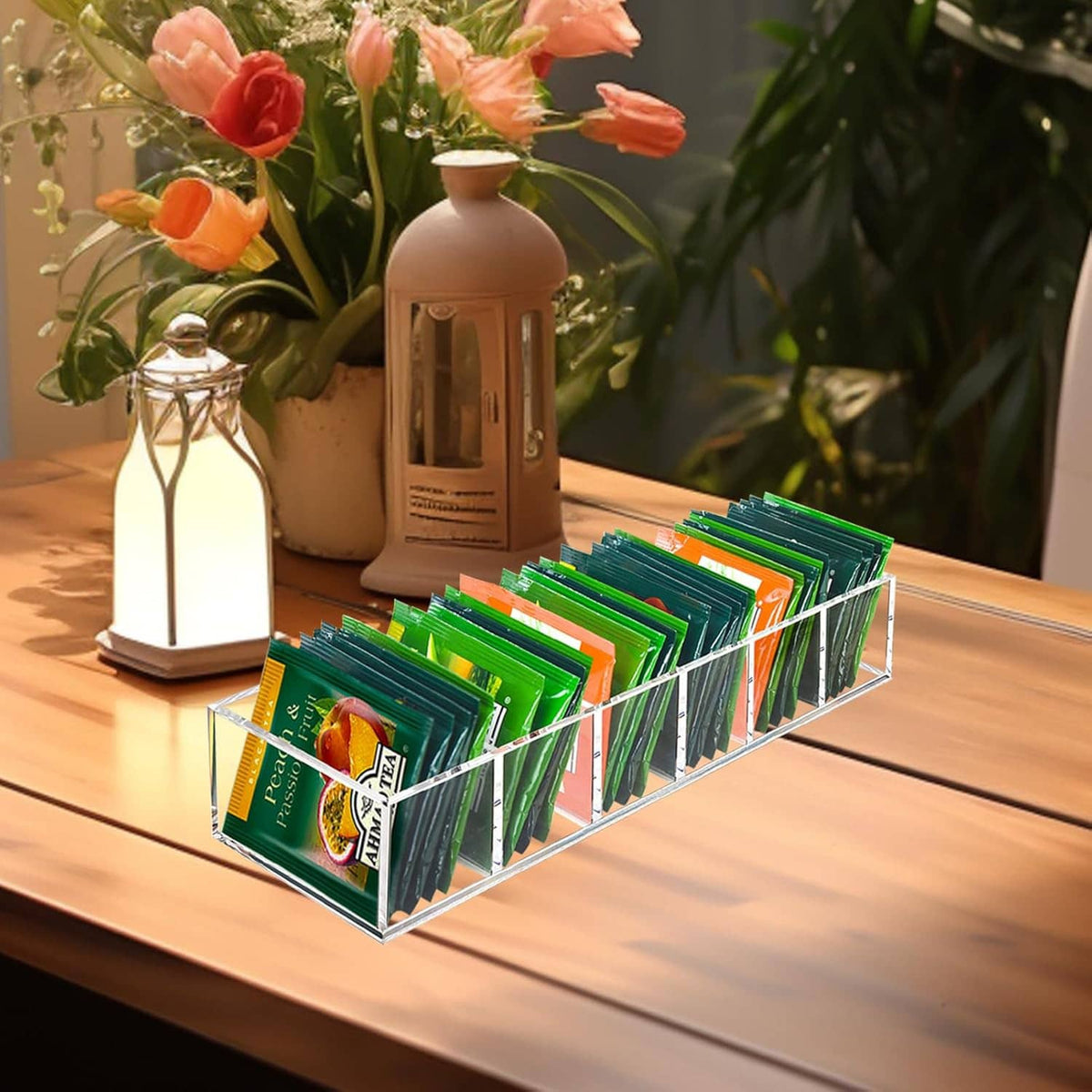 Clear acrylic tea bag organizer with slots holding green tea packets on a wooden table