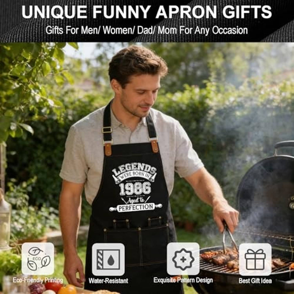 Black apron with printed 1986 design worn while holding a utensil near a grill.