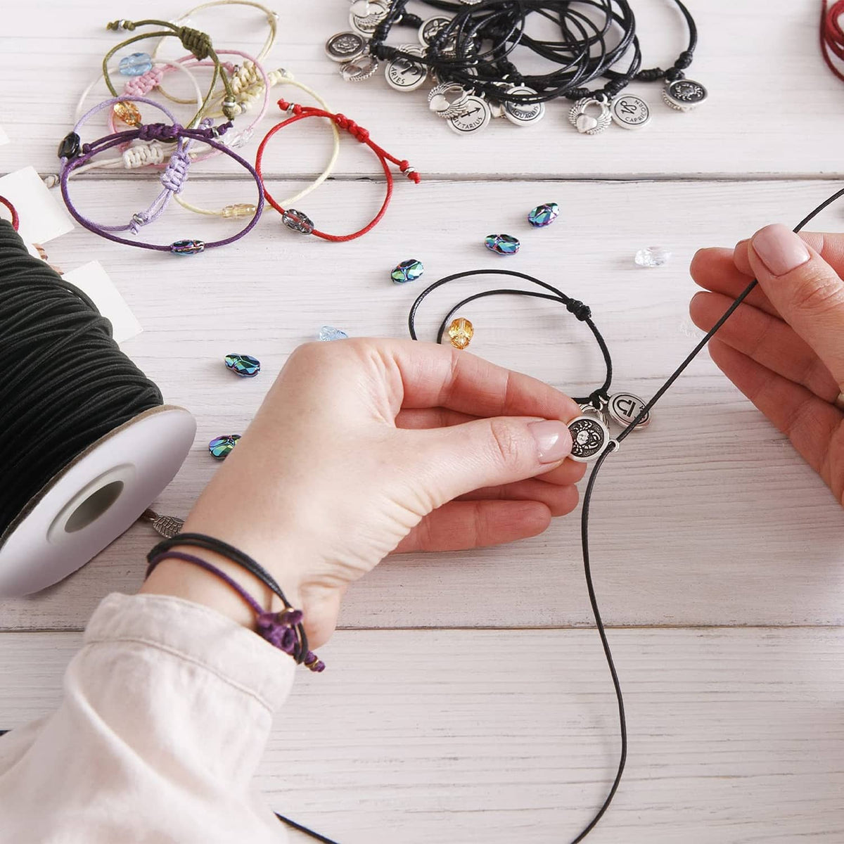 Black elastic cord for jewelry making, with hands threading through charms
