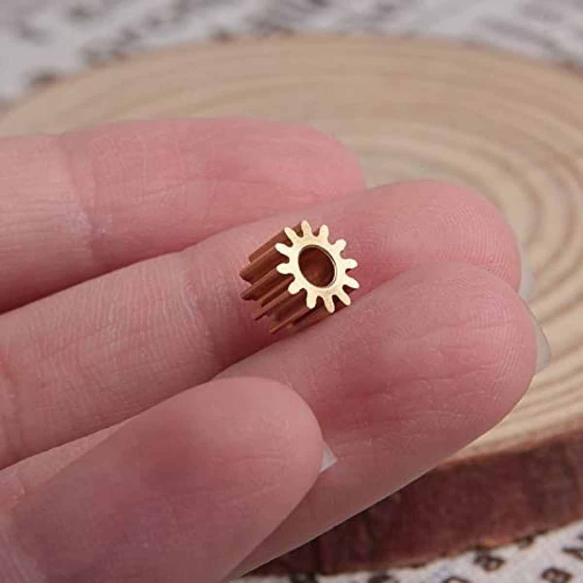 Gold 12-tooth spur gear with central 3 mm bore, close-up on fingers