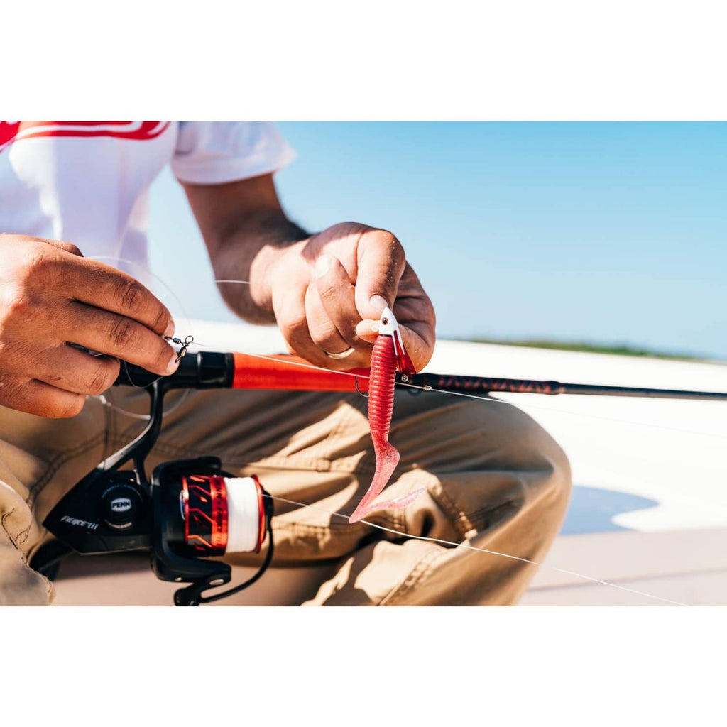 Red soft plastic worm lure on hook near fishing reel and rod