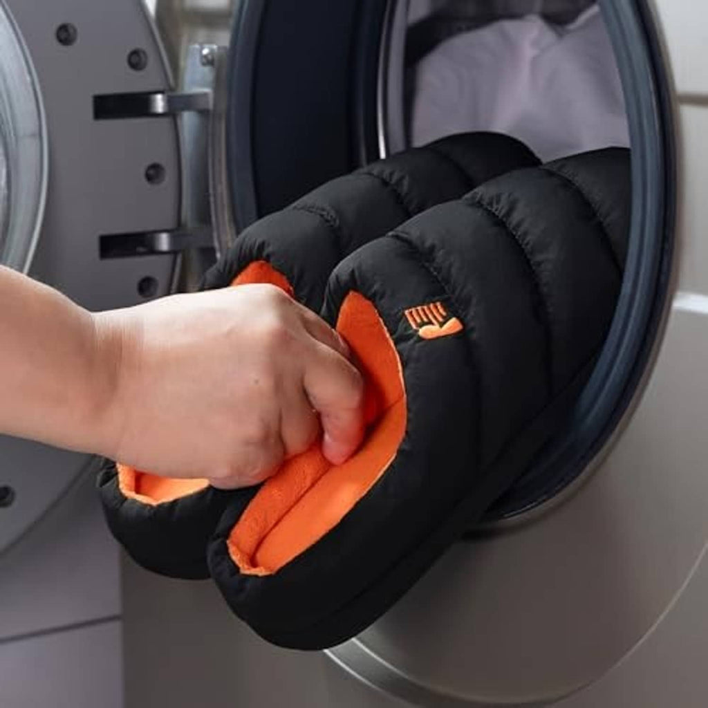 Men's black puffer slippers with orange lining being placed in a washer drum