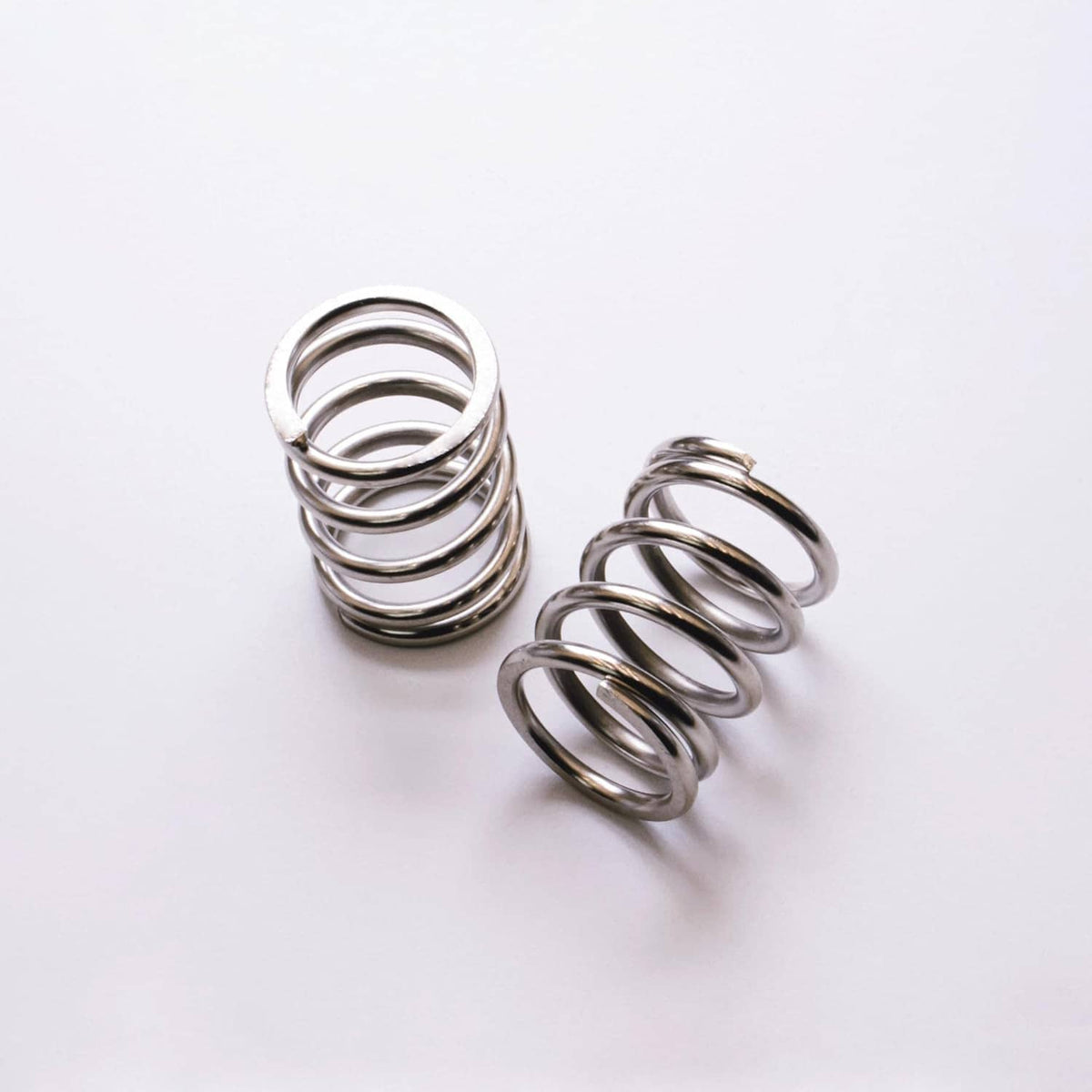 Nickel-plated valve springs, two coiled springs laid flat on a light background