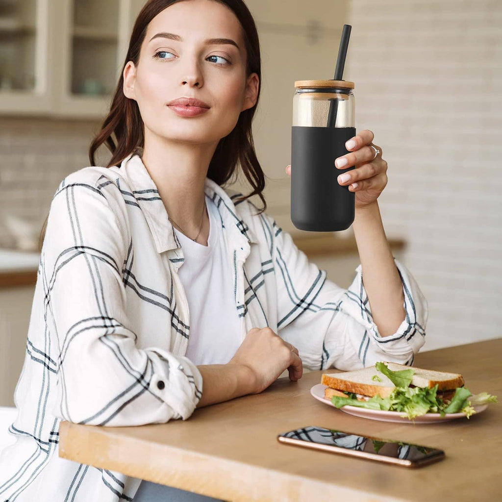 Black silicone-sleeved glass tumbler with straw, held on a cafe table