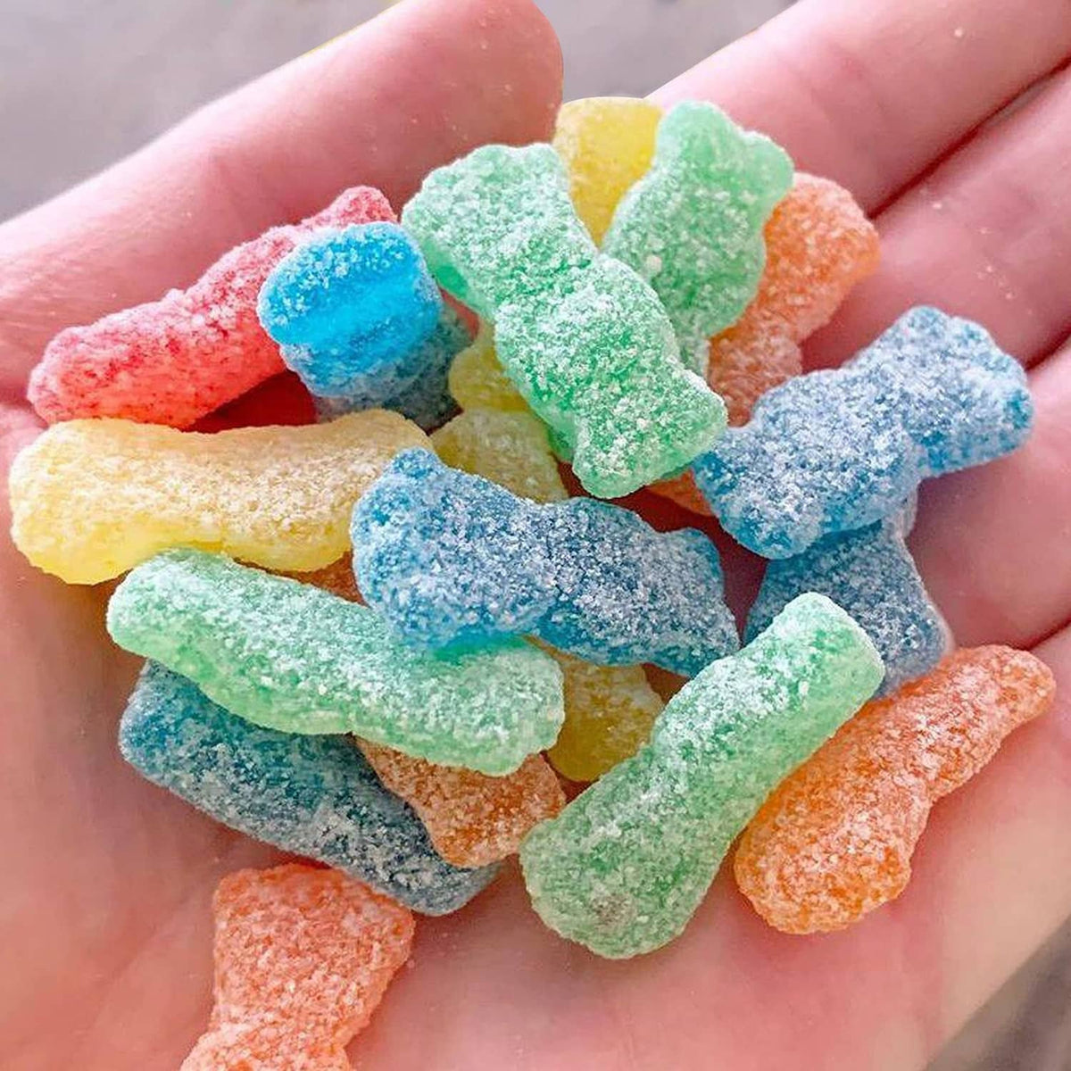 Hand holding assorted sour soft candy gummies in bright blue, green, orange, and red