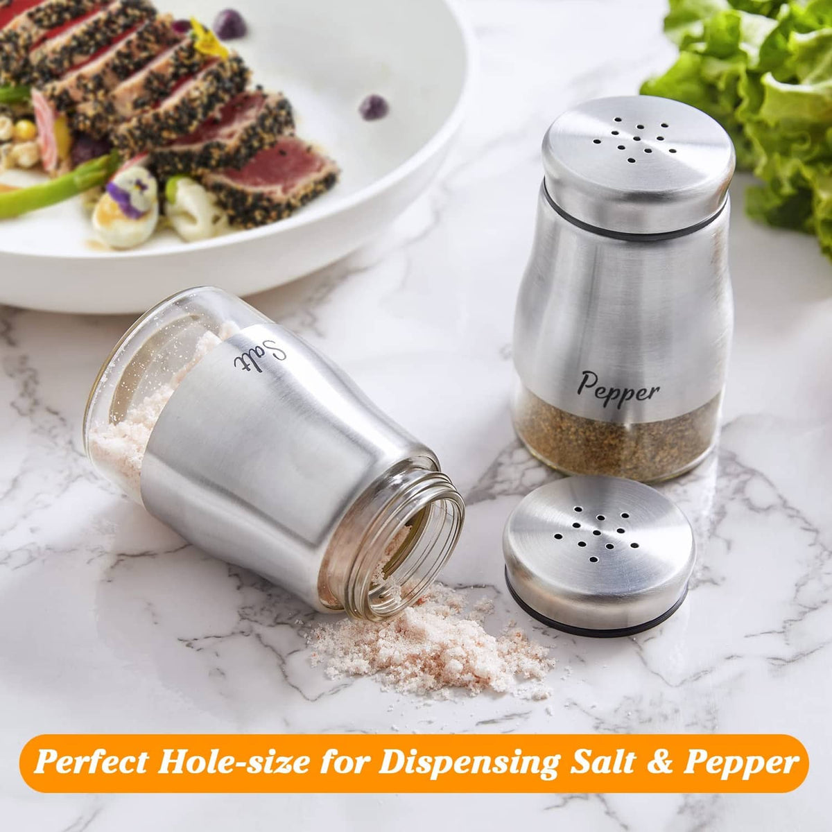 Stainless steel salt and pepper shakers, with one shaker tipped and seasoning spilled.