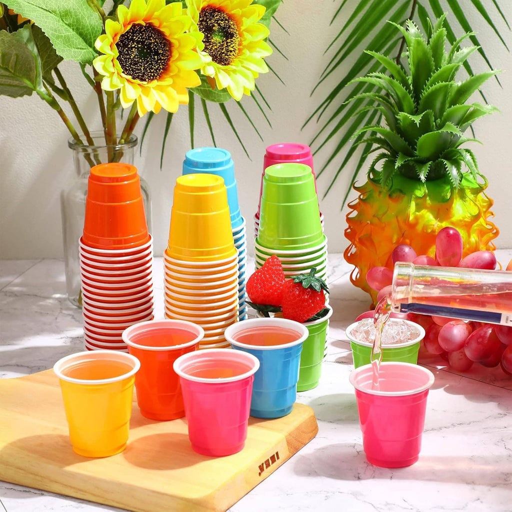 Assorted 2 oz plastic shot cups in orange blue yellow green, stacked on a wooden tray