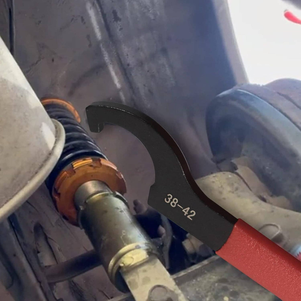 Red coilover spanner wrench fitting a shock strut on a vehicle suspension