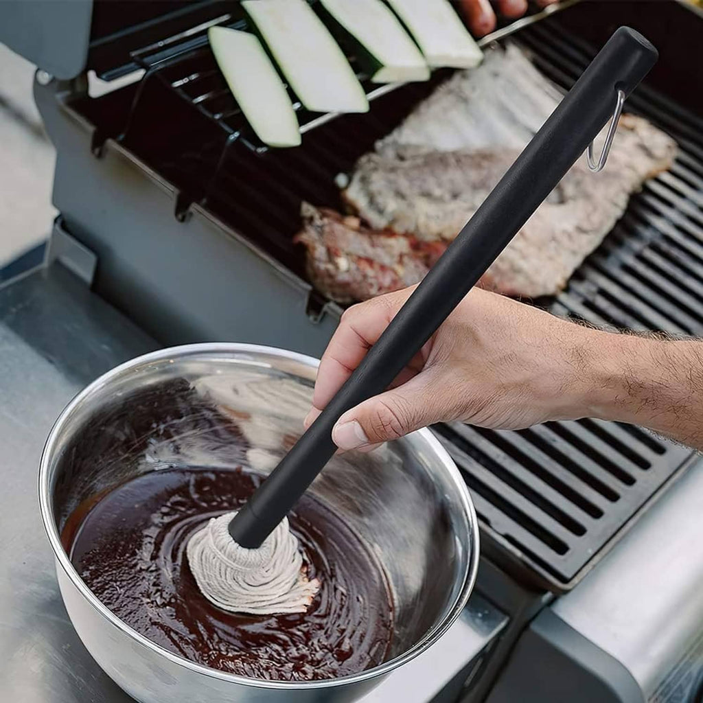 Hand holding grill basting mop handle while dipping tassel brush in sauce