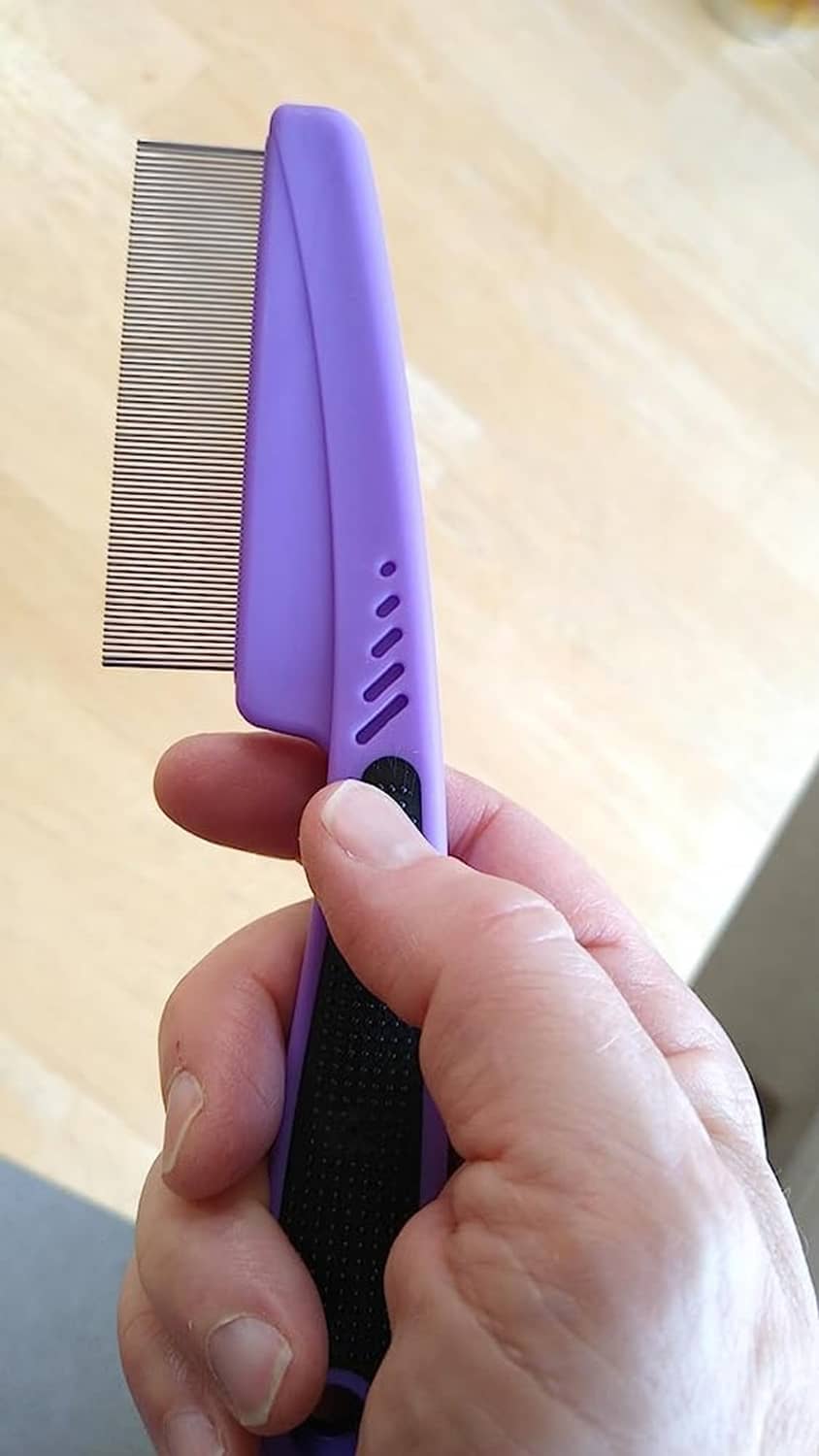 Purple flea comb with fine metal teeth and black textured grip, held in hand