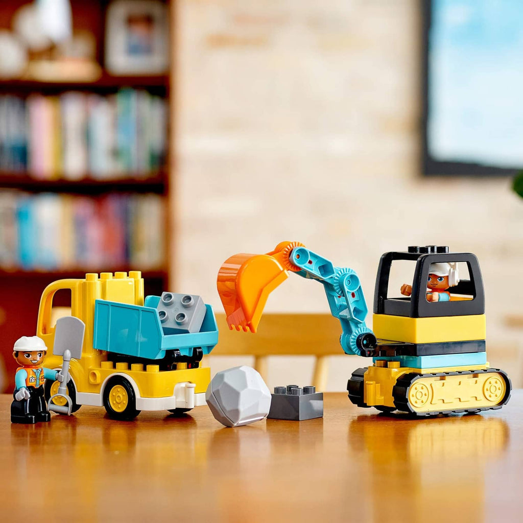 Side view of yellow truck and blue tracked excavator with worker figures and gray rocks