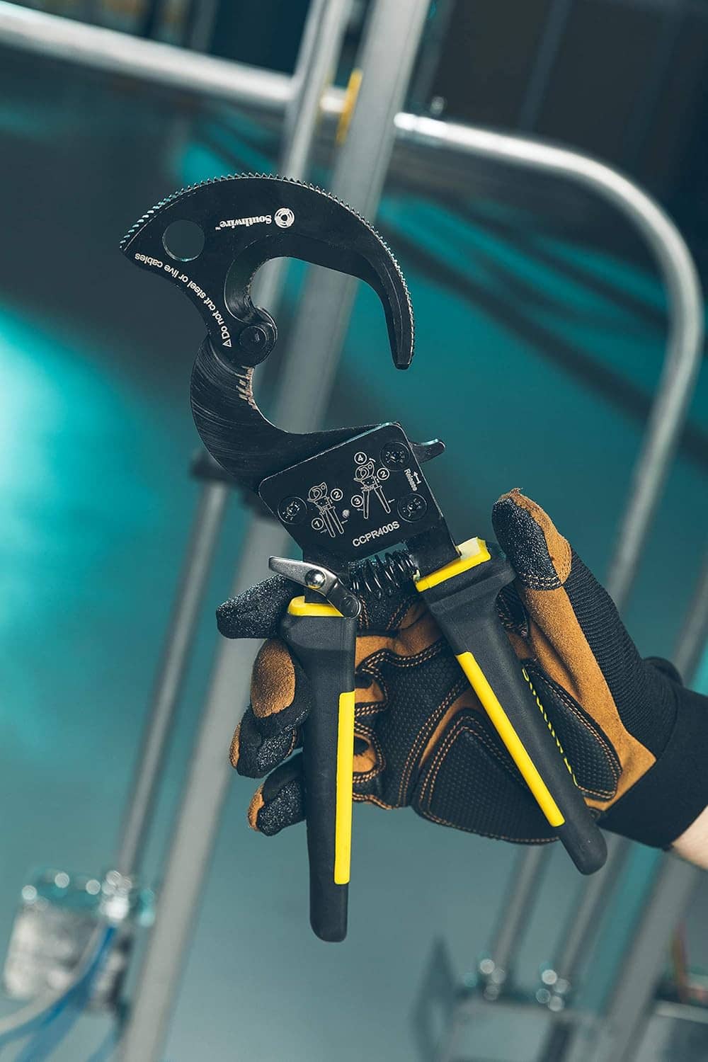 Ratcheting cable cutter tool with cutting jaw and yellow-black handles, in use
