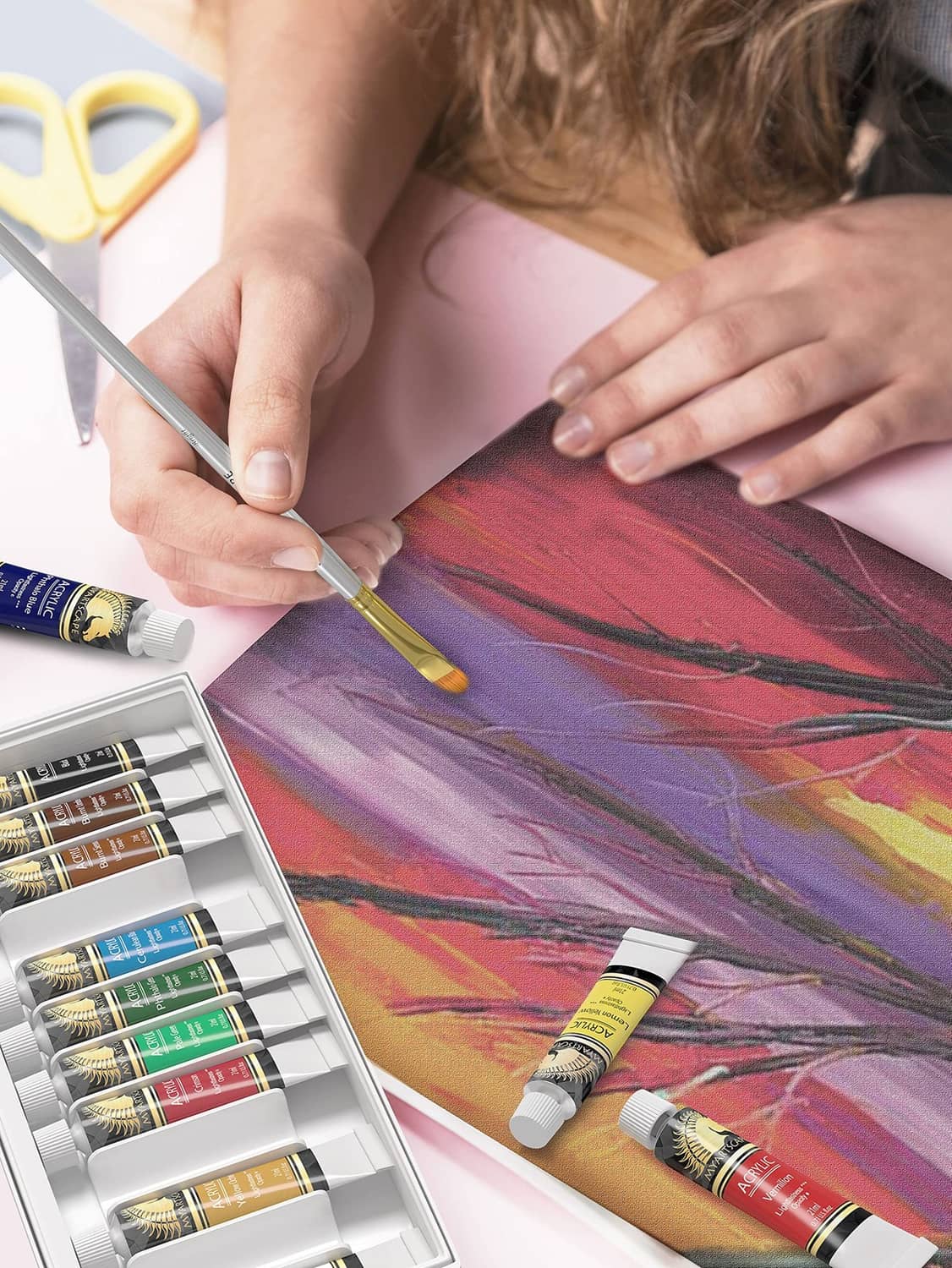 Person painting on canvas with acrylic brush and assorted paint tubes