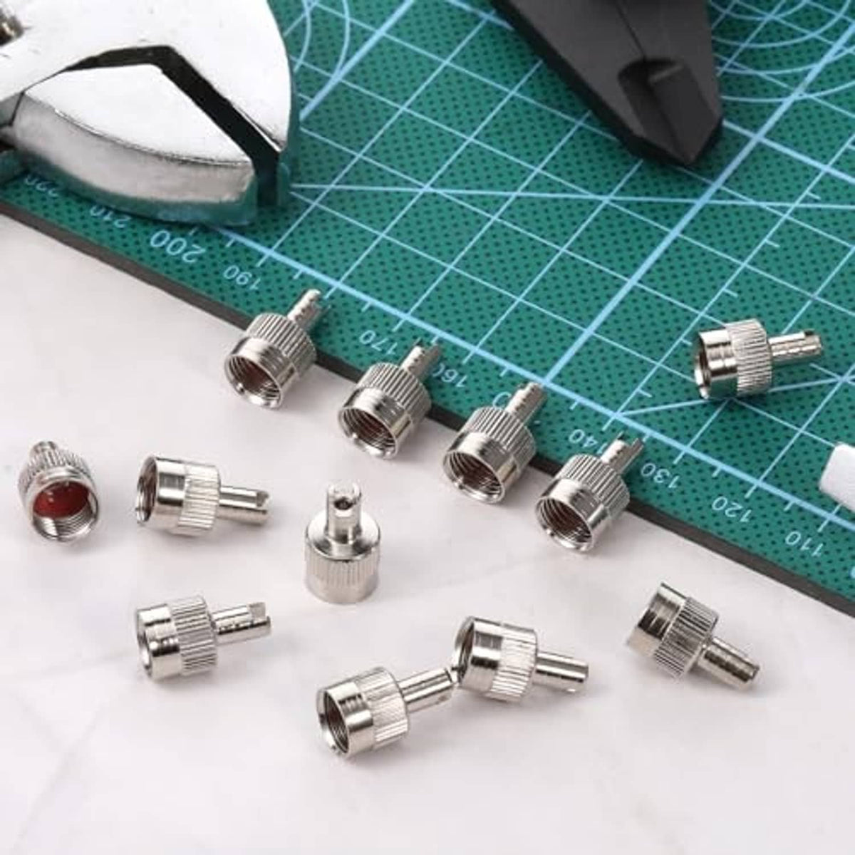 Assorted silver slotted tire valve stem caps with valve cores on a cutting mat