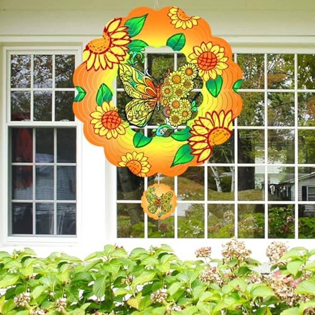 Butterfly wind spinner hanging in front of a window, orange floral petals with green leaves