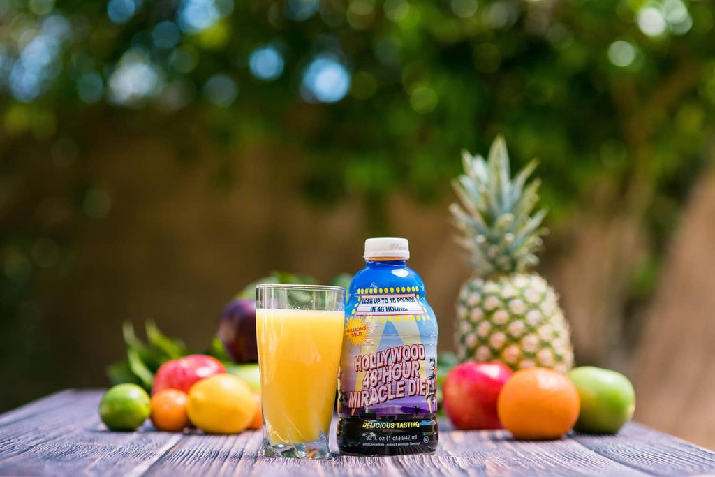 Fruit juice cleanse bottle with two glasses of orange juice and fresh produce