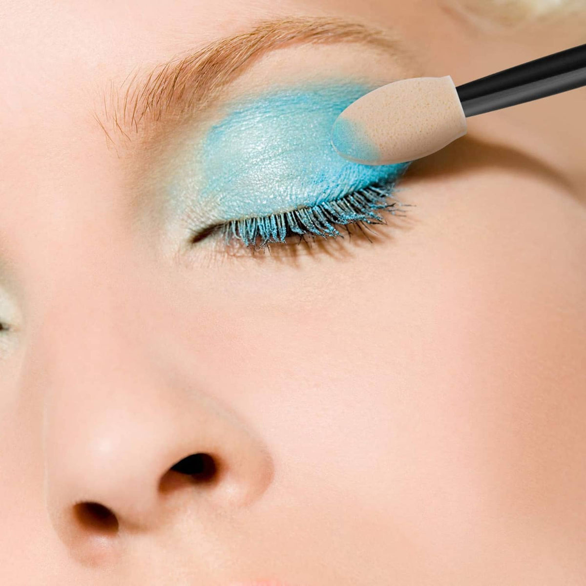 Disposable sponge applicator blending blue glitter eyeshadow on an eyelid