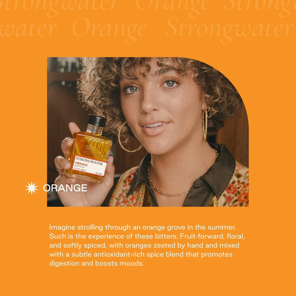 Orange bitters bottle held in hand by curly-haired person, drink in view