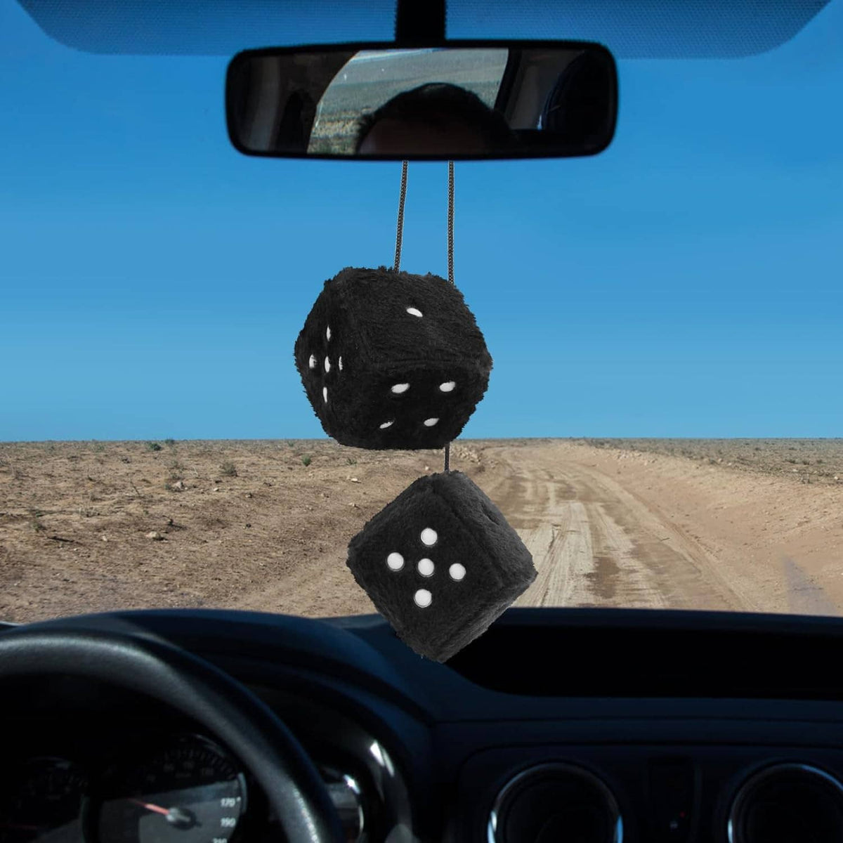 Pair of black fuzzy dice with white dots hanging from car mirror, dashboard view