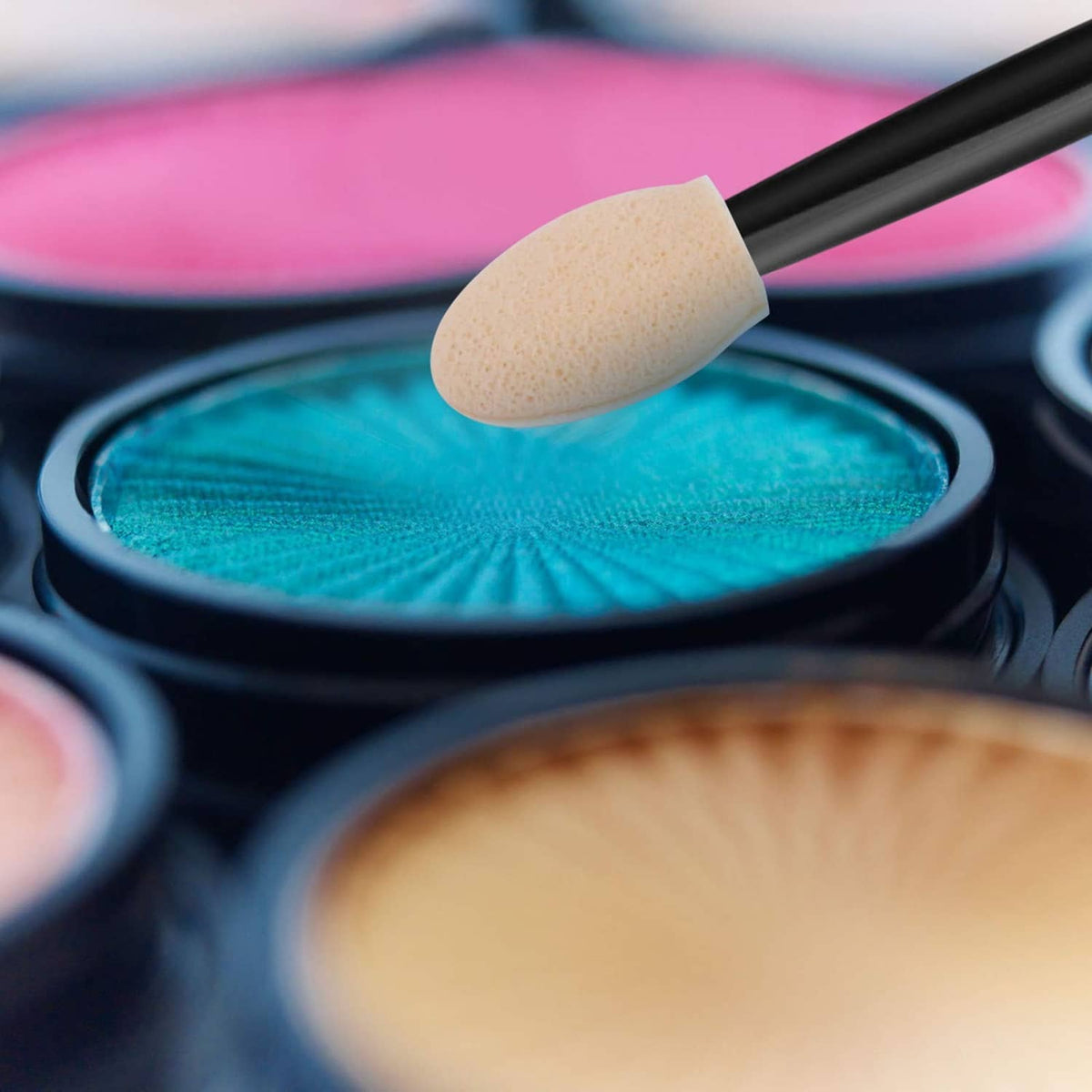 Sponge eyeshadow applicator applying turquoise blue eyeshadow from a black handle