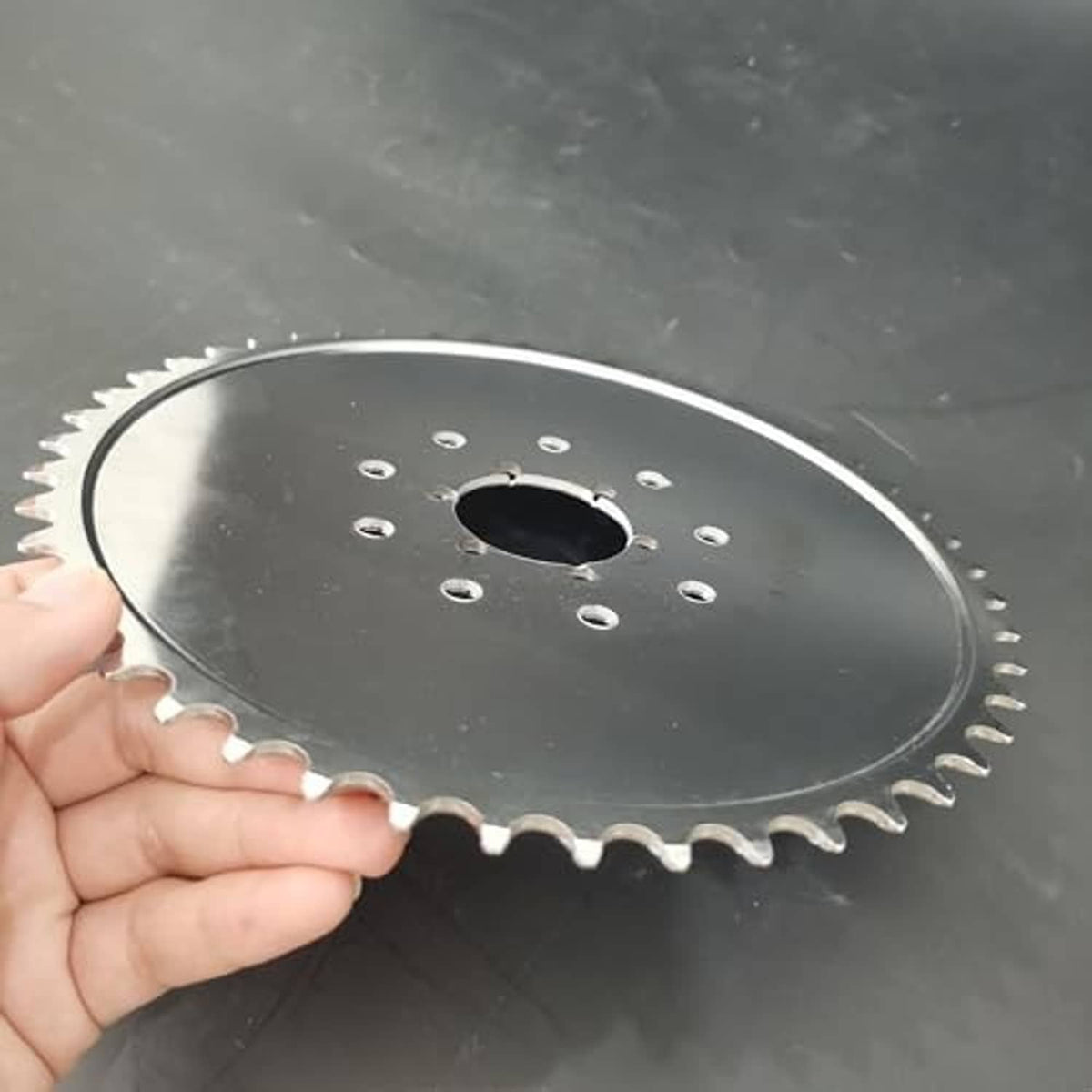 Steel sprocket held in hand, showing outer teeth and center mounting hole pattern