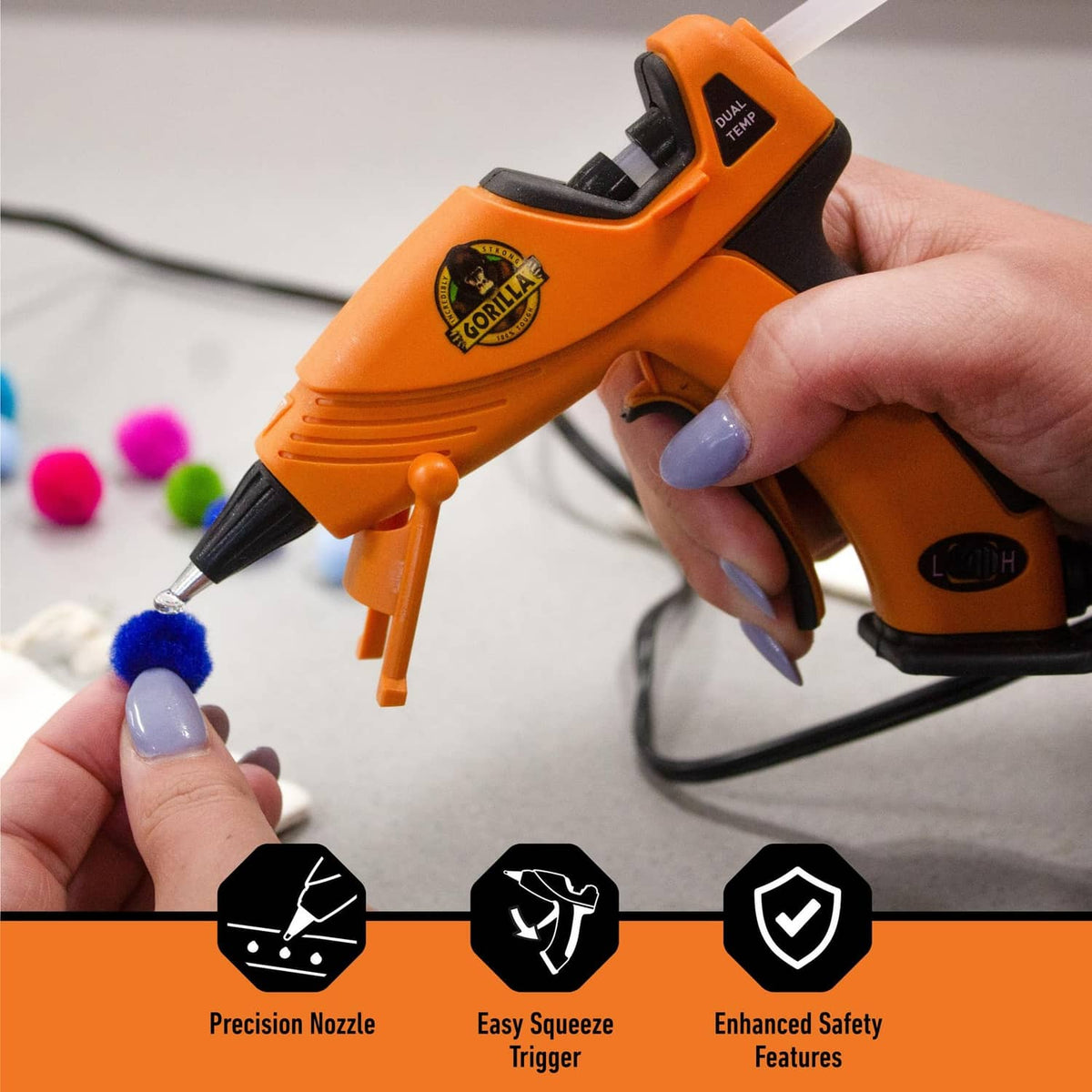 Orange mini hot glue gun held in hand with precision nozzle dispensing glue