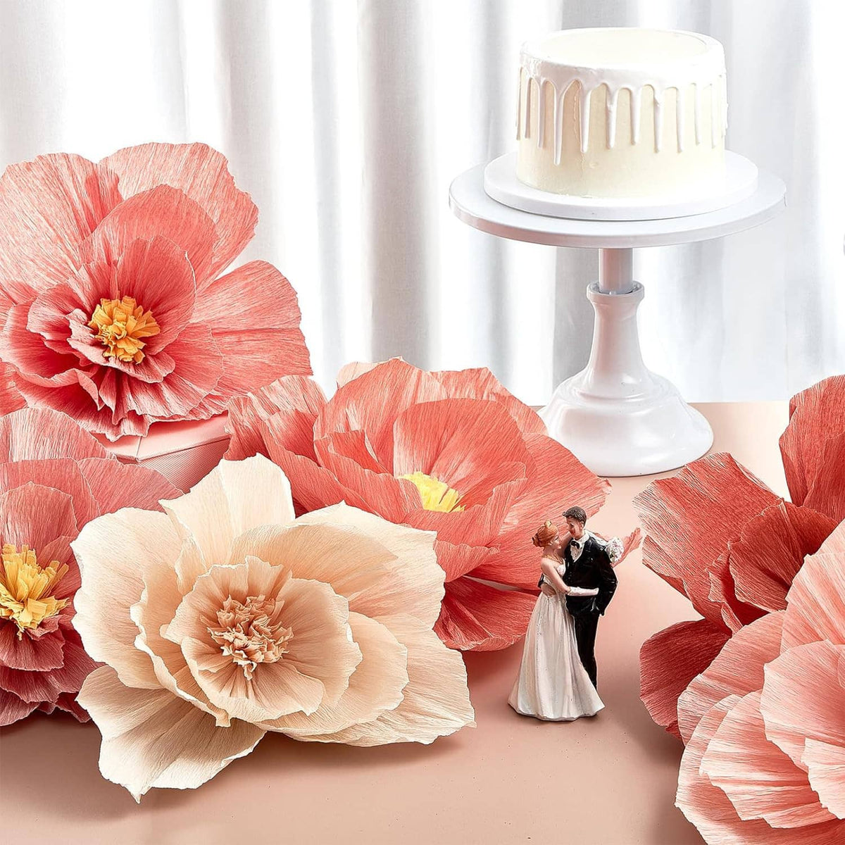 Coral and cream tissue paper flowers for wedding decor beside a white cake stand