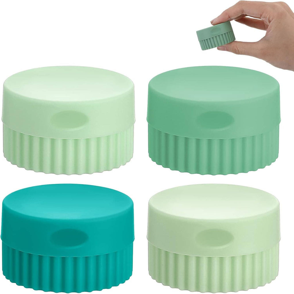 Four small silicone travel jars with ribbed sides and round caps, mixed green shades