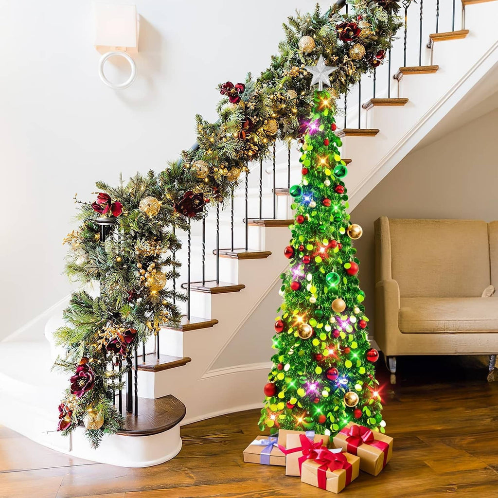 Lit green pop-up Christmas tree with star topper and colorful ornaments beside staircase