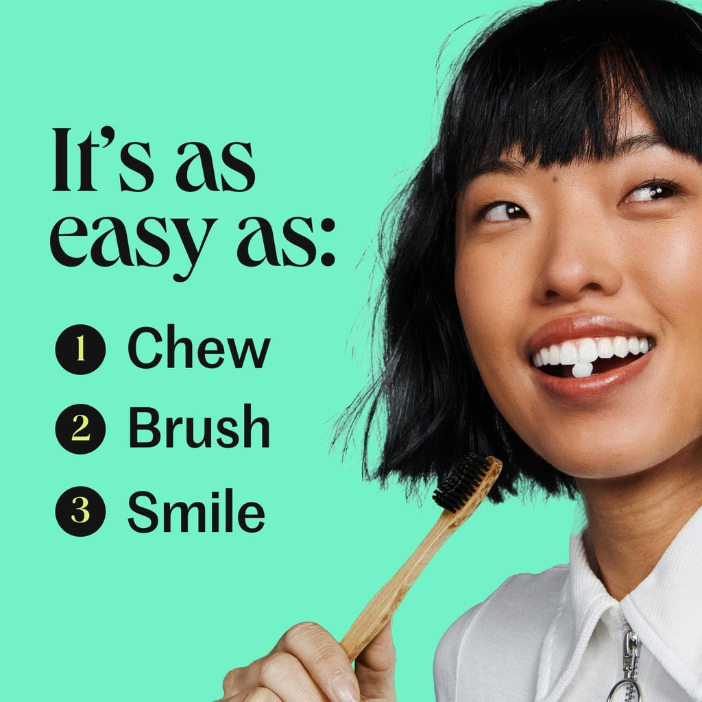 Smiling person with white tablet residue on teeth, holding a wooden toothbrush